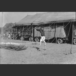 Man doing hand-stand on two tent pegs beside tent Ringling Bros