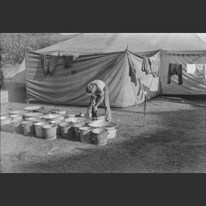 Man washing clothes beside tent buckets in fore-ground Ringling Bros